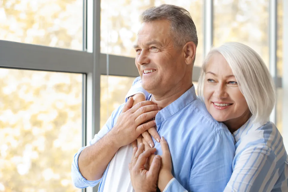 A happy retired couple embracing by a window
