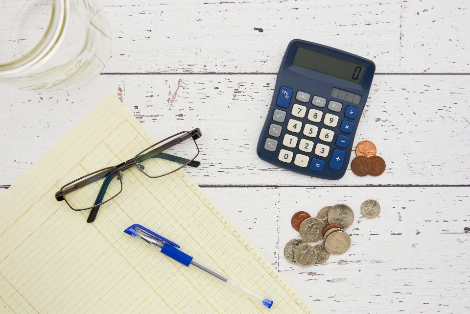 A calculator, glasses and coins on a desk